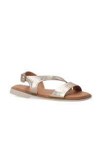 Metallisch gouden sandaal met kruisbandontwerp, een achterste sluiting met gespsluiting en een bruine, gevoerde binnenzool op een lichte rubberen outsole.