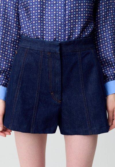 Shorts de mezclilla de talle alto, color azul oscuro y costuras naranjas contrastantes. Cuenta con un bolsillo lateral y un ajuste estructurado.