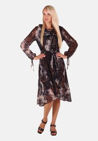 Schwarzes und braunes abstraktes Drucklangarmkleid mit Taillenschnürung, fließendem Stoff und transparenten Details. Kombiniert mit schwarzen Plateau-Sandalen.