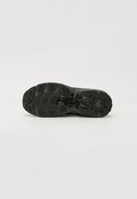 Black athletic shoe outsole featuring textured rubber with varied traction patterns and a logo. The design emphasizes durability and grip.