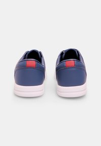 Sneaker in pelle sintetica blu con suola bianca, accento rosso sul retro e texture liscia. Progettati con un profilo basso.