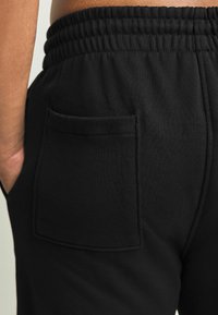 Schwarze Jogginghose mit weicher Textur, elastischem Bund und einer einzelnen Gesäßtasche. Schlichtes Design mit minimalen Details.