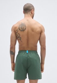 Πράσινα μαγιό σορτς με ελαστική μέση και μπλε κορδόνι. Το ύφασμα φαίνεται ελαφρύ και λείο, σχεδιασμένο για άνεση και κινητικότητα.