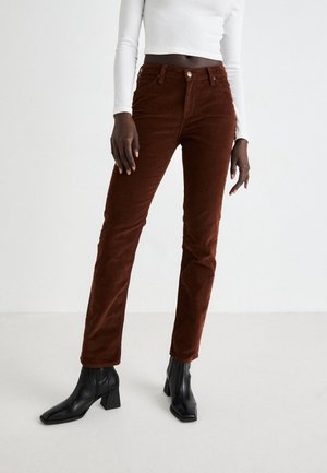 Pantaloni in corduroy marroni con una vestibilità slim, dotati di passanti per cintura e chiusura con bottone frontale, abbinati a stivaletti neri con tacco.