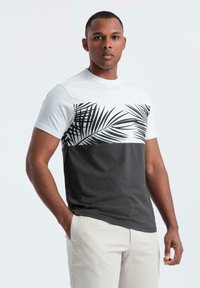 Triko s krátkým rukávem s bílou horní částí, na které je černý potisk palmového listu, a tmavě šedou dolní částí; vyrobeno z hladkého materiálu.