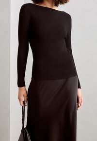 Haut noir à manches longues côtelé avec un large décolleté, associé à une jupe noire élégante. Le tissu semble doux et ajusté.