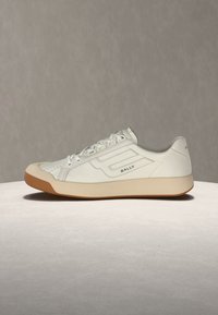 Baskets basses en cuir blanc avec semelle beige, bout perforé, fermeture à lacets à l'avant, et logo Bally sur le côté et le talon.