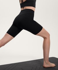 Svarta högmidjade cykelshorts gjorda av stretchigt tyg, med en slät yta och en figurnära design, använda på en yogamatta.