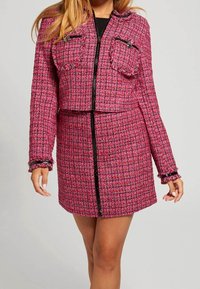 Roze tweedjack met twee voorzakken, een cropped ontwerp en rafelige mouwen. Voorzien van een zwarte rits en een gemêleerd stofpatroon.