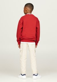 Felpa rossa con collo rotondo, abbinata a pantaloni cargo beige. Il bambino indossa sneakers bianche con dettagli blu navy e un colletto a righe.