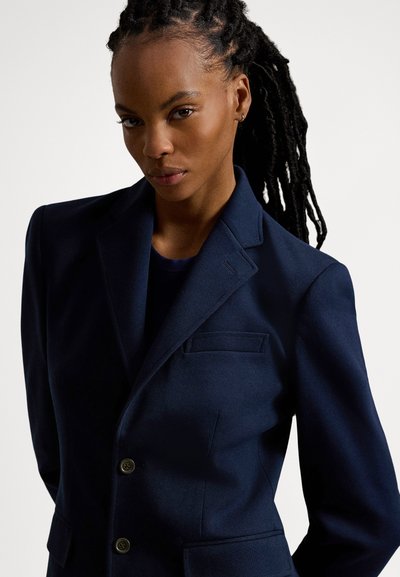 Ναυτικό μπλέ σακάκι από απαλό ύφασμα, με μονόπετο σχέδιο, δύο κουμπιά στο μπροστινό μέρος και μια τσέπη στο στήθος. Με εφαρμοστή γραμμή.