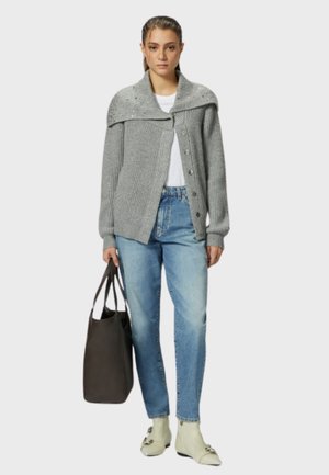 Cardigan grigio a maglia con ampio colletto, bottoni e texture a coste, abbinato a jeans azzurri chiari e stivaletti beige. Tiene una borsa scura.