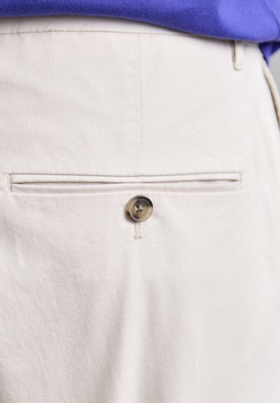 Beige cotton trousers featuring a button closure, flat front pocket, and contrasting stitching detail. The fabric has a smooth texture.