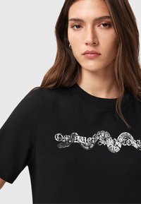 T-shirt in cotone nero con una grafica di un serpente intrecciato con testo stilizzato. Maniche corte, scollatura rotonda, vestibilità casual.