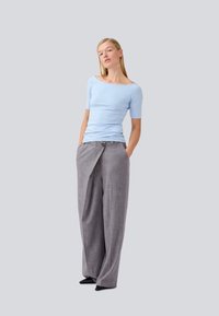 Lichtblauw, kort mouwtopje gecombineerd met grijze, wijde geruite broek met knoopdetail en voorraffing. Zwarte puntige schoenen.