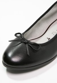 Ballerines en cuir noir avec un bout arrondi, présentant une surface texturée et un nœud en décoration à l'avant. Doublure intérieure lisse.