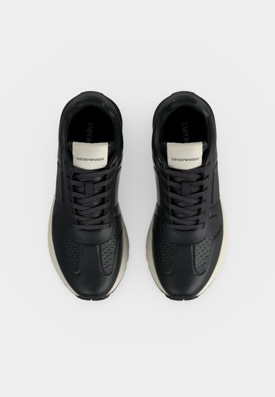 Paire de baskets noires et blanches Emporio Armani vues de dessus, avec lacets noirs et étiquettes de languette à la marque.