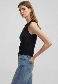 Top sin mangas negro acanalado con costuras decorativas en el hombro, combinado con unos pantalones vaqueros de cintura alta de color azul claro. Textura suave, diseño ajustado.