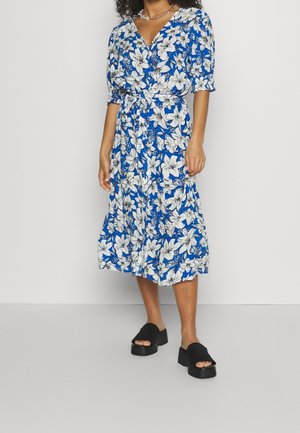 Abito floreale blu con maniche a sbuffo corte, chiusura con bottoni e cintura in vita. Presenta fiori bianchi su sfondo blu. Sandali platform neri.