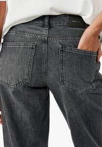 Jeans negros con un diseño clásico de cinco bolsillos, con cintura alta y pierna recta, hechos de una tela de denim texturizada.