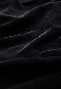 Mustast sametist kangas, millel on pehme, sile tekstuur, sügavad voltid ja peened valguse peegeldused kogu pinnal.