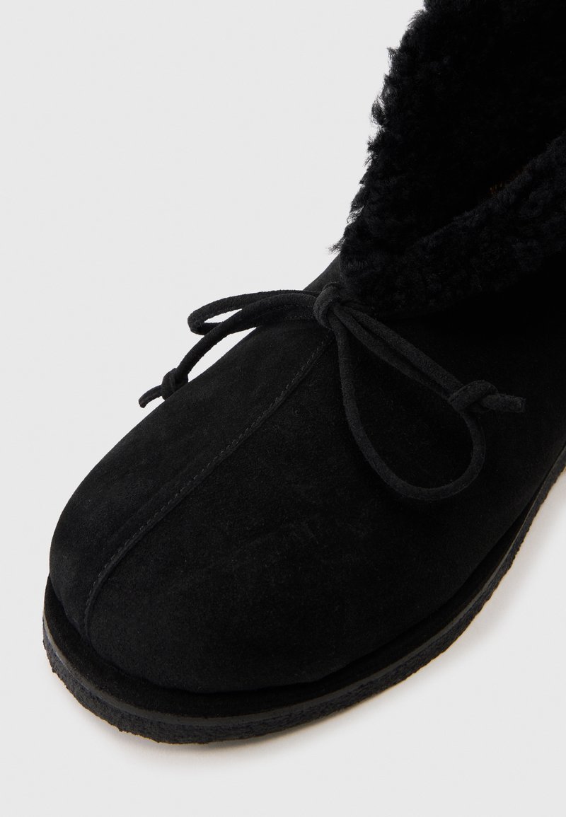 Botte d'hiver en suède noir avec doublure en fausse fourrure et lacets noués sur fond blanc, montrant les détails avant et latéraux.