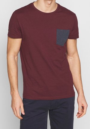 T-shirt corta bordeaux in tessuto morbido con collo rotondo e taschino sul petto blu scuro, caratterizzato da una vestibilità classica e una texture liscia.