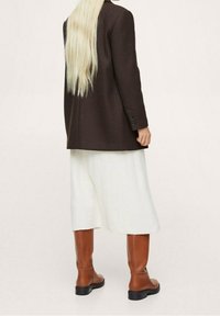 Brown wool blazer, cream pleated mid-length skirt, and knee-high brown leather boots. Textured fabric and tailored design.