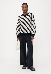 Maglione a righe bianche e nere in maglia con una vestibilità ampia, abbinato a pantaloni neri a gamba larga e scarpe con zeppa. Tiene una piccola borsa bianca.