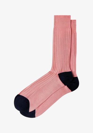 Par de calcetines rosados con costillas, con talones y punteras negras sólidas, colocados planos y superpuestos sobre un fondo blanco.