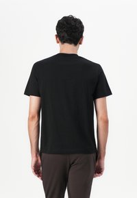 Schwarzes T-Shirt mit kurzen Ärmeln und Rundhalsausschnitt, aus glattem Stoff gefertigt. Der Rücken ist schlicht ohne Grafiken oder Verzierungen, kombiniert mit braunen Hosen.