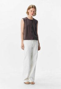 Top gris sans manches avec un col rond et un bouton à l'avant, associé à un pantalon large blanc et des sandales plates. Design simple et structuré.