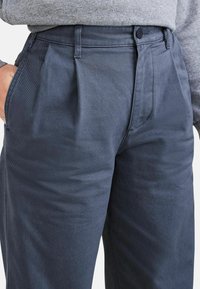 Mörkblå plisserade byxor i en bomullsblandning, med knäppning och sidfickor, med en mjuk yta och en strukturerad design.