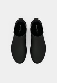 Pantofi negri slip-on cu o finisare mată netedă, vârfuri rotunjite și un design minimalist. Dotati cu o bucată de prindere pentru a fi ușor de încălțat.