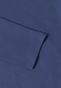 Gros plan sur le poignet et la couture de la manche d'une chemise à manches longues bleue, montrant des coutures fines et une texture de tissu lisse.