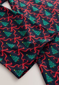 Tissu bleu marine avec un motif festif de sapins verts et de volutes de rubans rouges, agrémenté d'étoiles jaunes. Texture douce et à motifs.