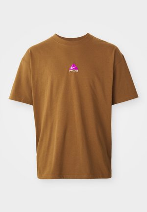 Brun bomulds t-shirt med rund hals. Har et lille pink og lilla ACG-logo på brystet. Korte ærmer, standard fit, glat tekstur.