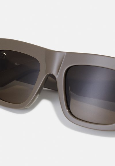 Ochelari de soare din plastic maro, cu rame mari, pătrate. Lentile întunecate, cu o textură netedă și detalii minime pe laterale.