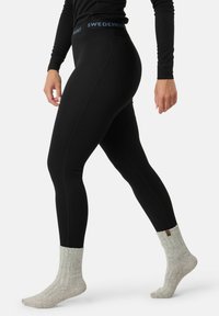 Schwarze gerippte Leggings mit hohem Bund, auf dem der Text "SWEDEMOUNT" steht, kombiniert mit grauen gestrickten Socken mit umgeschlagenem Saum.