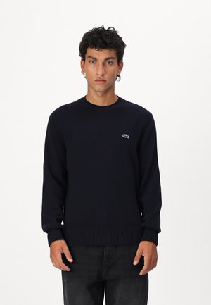 Navy blue knit sweater with crew neckline, ribbed cuffs and hem, featuring a small green crocodile logo on the left chest.