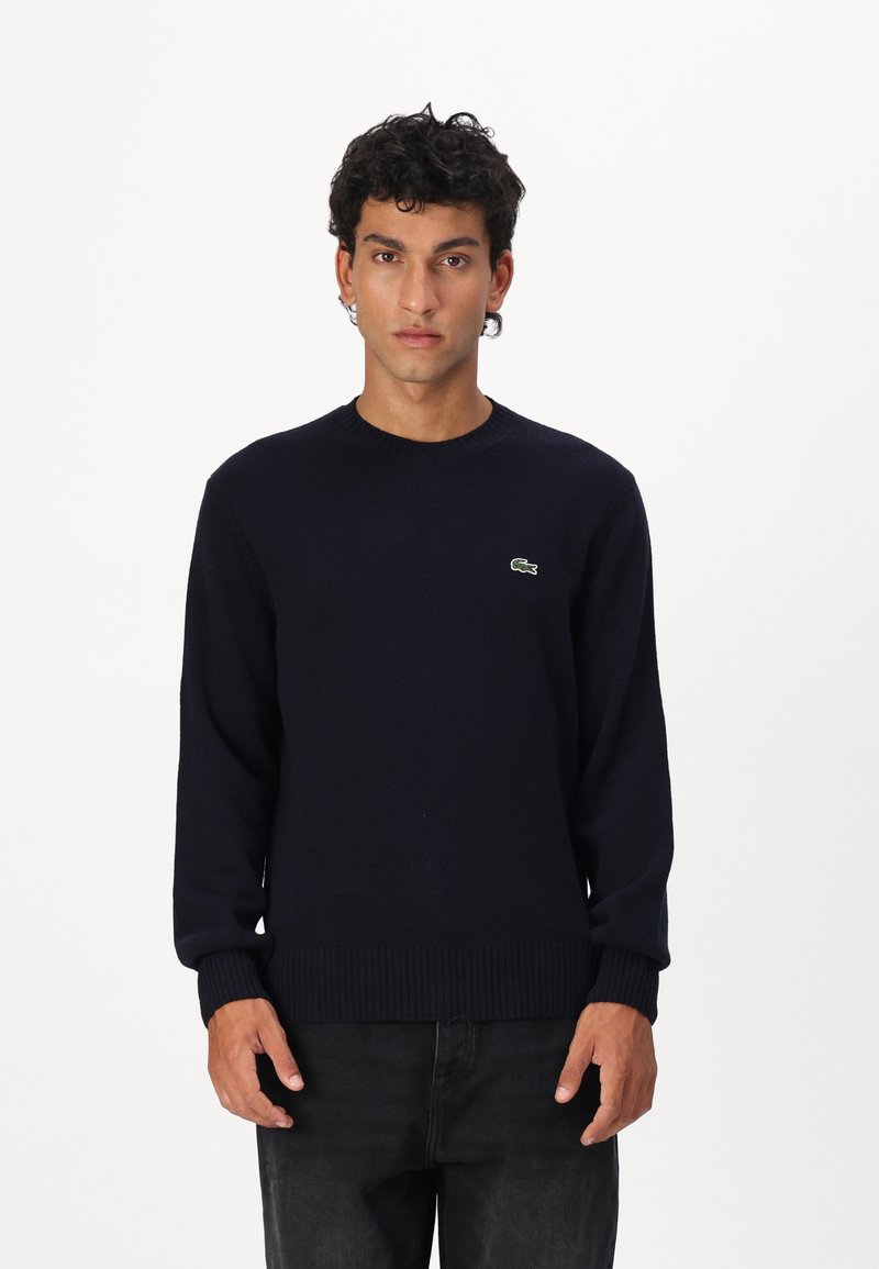 Ναυτικό μπλε πλεκτό πουλόβερ με στρογγυλή λαιμόκοψη, ριχτές μανσέτες και τελείωμα, που διαθέτει ένα μικρό πράσινο λογότυπο κροκόδειλου στο αριστερό στήθος.