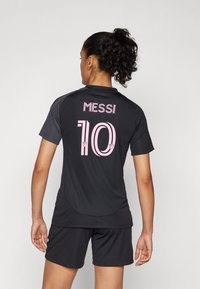Black athletic jersey featuring pink "MESSI" text and the number "10" on the back, paired with black shorts. Smooth fabric, short sleeves.
