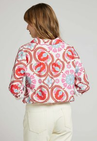 Chemise à manches courtes avec un motif floral à l'arrière en rouge, rose et bleu sur fond blanc, fabriquée en tissu léger.
