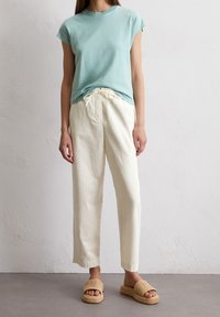 T-shirt di cotone blu chiaro, pantaloni di lino bianchi con vita elastica e sandali a infradito intrecciati beige con suola piatta.
