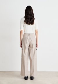 Beige cargobroek gemaakt van geweven stof, met wijde pijpen, zijzakken en een gladde afwerking. Gemonteerd met een aansluitend wit t-shirt met korte mouwen.