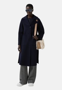 Marineblauwe wollen jas met een brede kraag, knoopsluiting en zakken. Gecombineerd met gestreepte broeken en een kleine beige tas met dierenvachtaccenten.