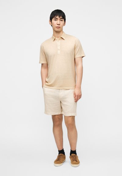 Μπεζ πουκάμισο πόλο με κοντή πατιλέτα, σε συνδυασμό με ανοιχτό μπεζ σορτς. Το σύνολο διαθέτει άνετη εφαρμογή, υφή σαν βαμβάκι και καφέ παπούτσια.