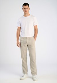 Witte t-shirt met korte mouwen, gecombineerd met lichtbeige gestreepte broek. Model draagt witte sneakers. Eenvoudig ontwerp, geen zichtbare patronen of logo's.
