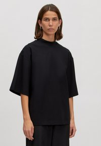 Zwarte oversized katoenen T-shirt met korte mouwen, hoge kraag en een relaxte pasvorm. Soepele textuur zonder zichtbare patronen of accenten.