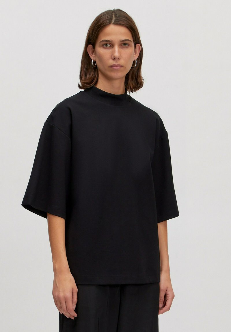 Zwarte oversized katoenen T-shirt met korte mouwen, hoge kraag en een relaxte pasvorm. Soepele textuur zonder zichtbare patronen of accenten.